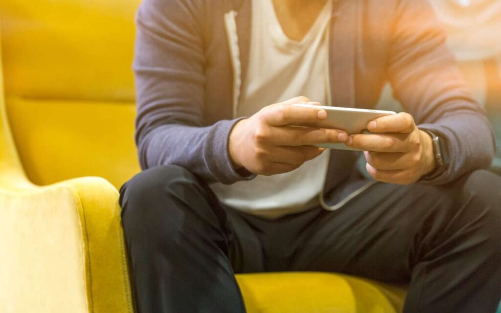 Čovek koristi telefon dok sedi na žutoj fotelji