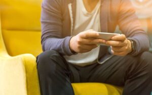Čovek koristi telefon dok sedi na žutoj fotelji
